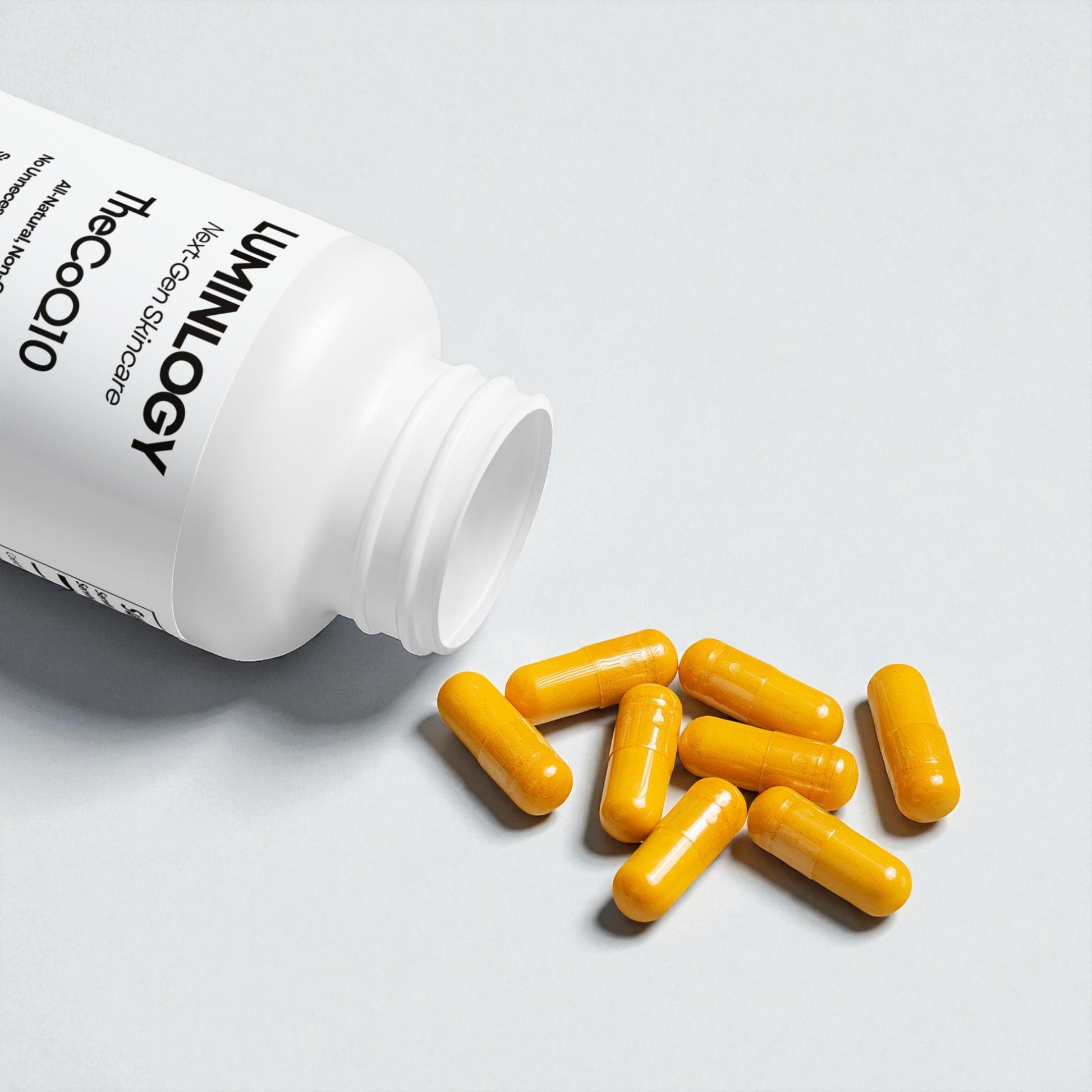 Yellow CoQ10 capsules spilling out of a white bottle of "Luminlogy supplements" on a light surface.