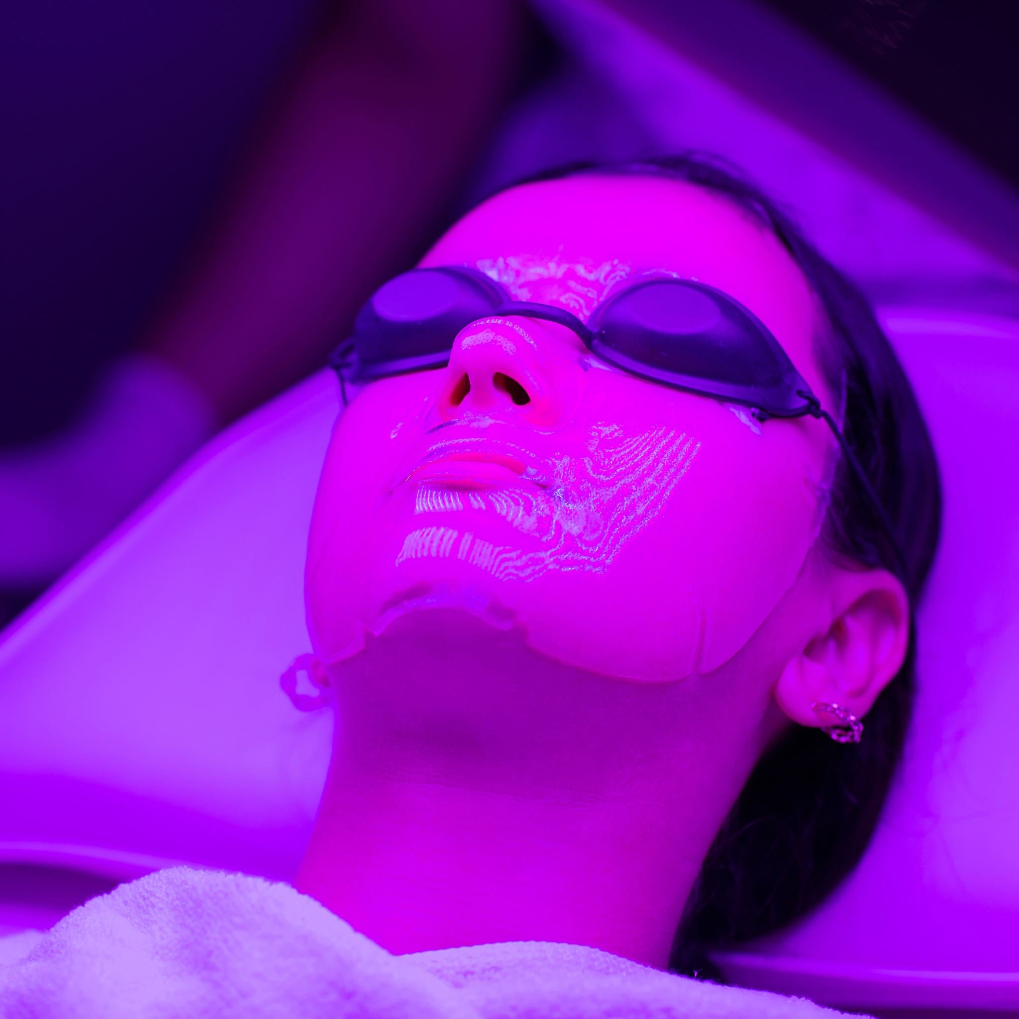 A woman using purple LED light therapy on her face as she is laying down.