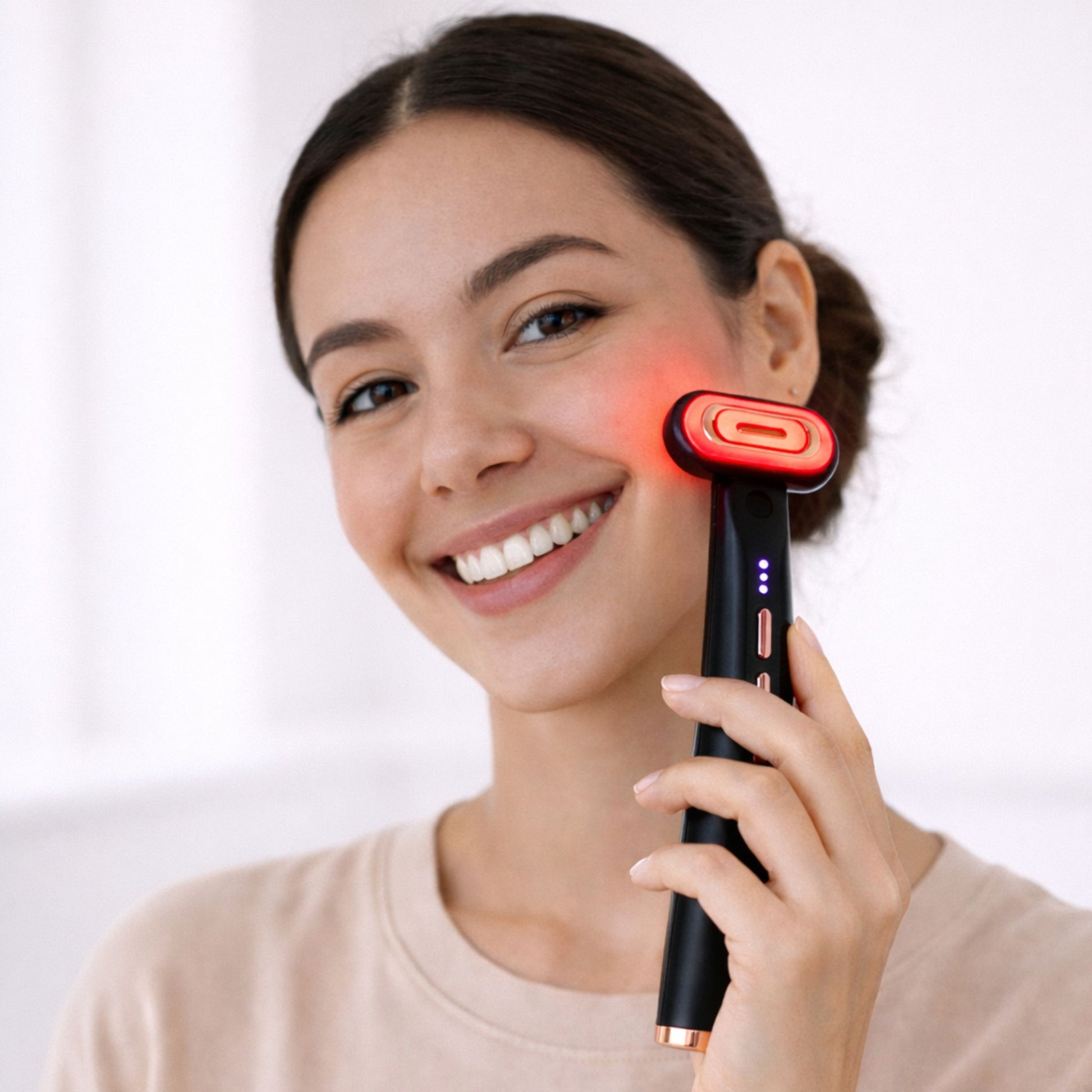 A woman using the anti-aging red light therapy wand on her face while smiling. 